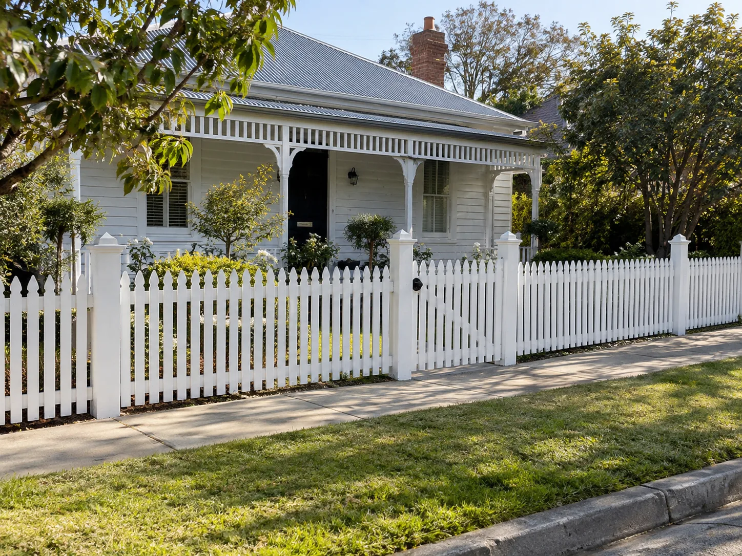 White picket fence and gate in front of a veranda house.